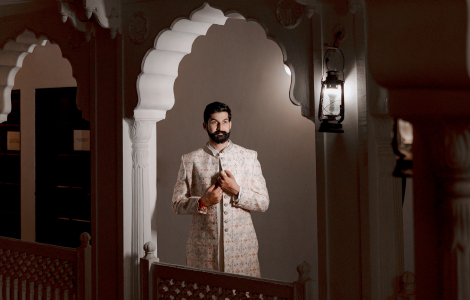 A groom in a white sherwani stands in a doorway.