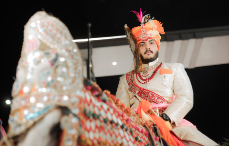 A man dressed in Indian wedding attire rides a horse.