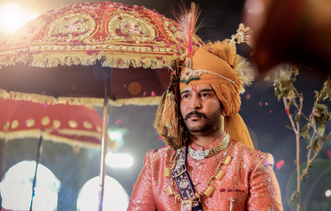 A groom wearing a traditional Indian outfit stands with an umbrella.