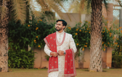 A groom in traditional Indian clothing stands on the grass.