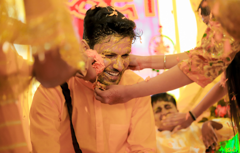 A groom having his face painted orange, capturing the vibrant essence of Haldi Photography.
