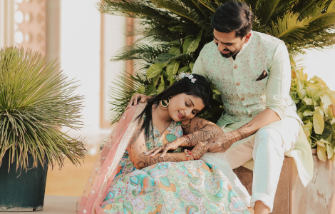 A couple dressed in traditional Indian wedding attire, showcasing intricate mehendi designs on their hands.