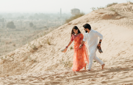 A couple strolls hand in hand across the golden sand dunes of Jaisalmer, enjoying the serene desert landscape.