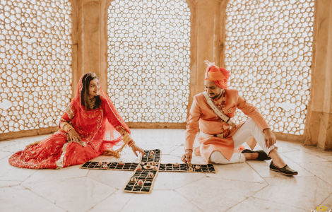 A couple in traditional Indian attire joyfully playing dominoes during their pre-wedding photoshoot.