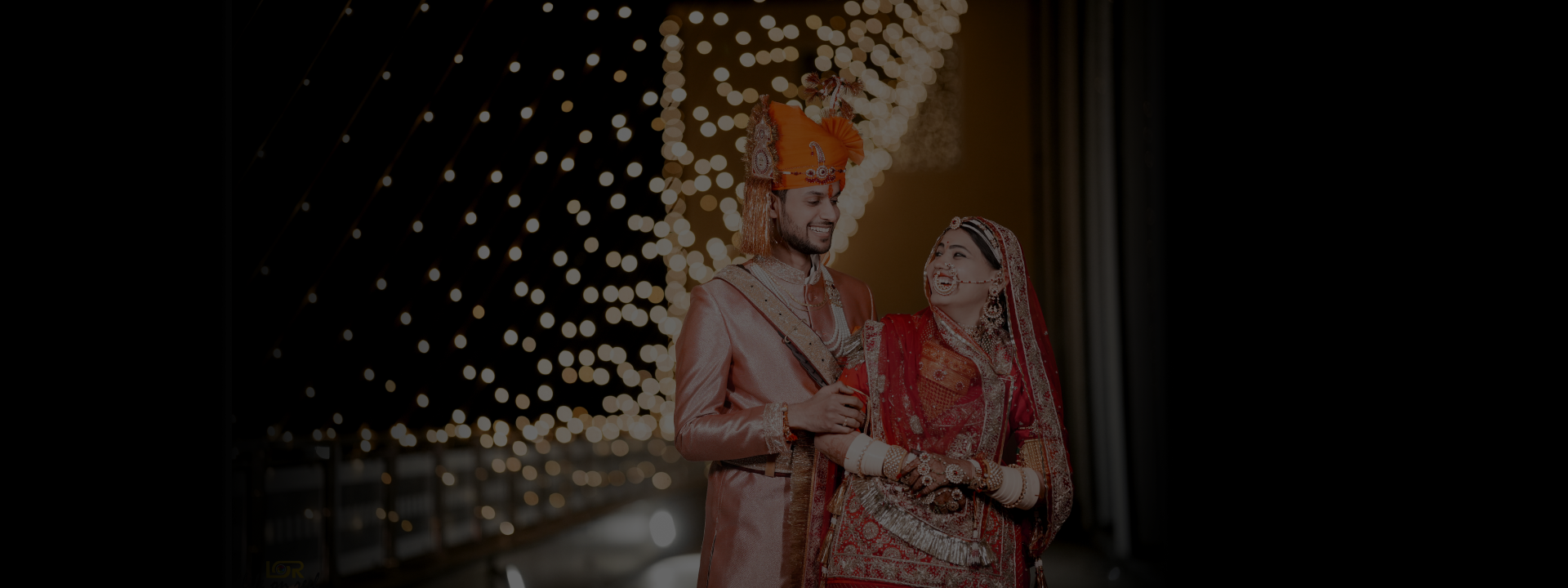  A couple dressed in traditional Indian attire poses in front of a beautifully lighted backdrop, radiating joy and elegance.