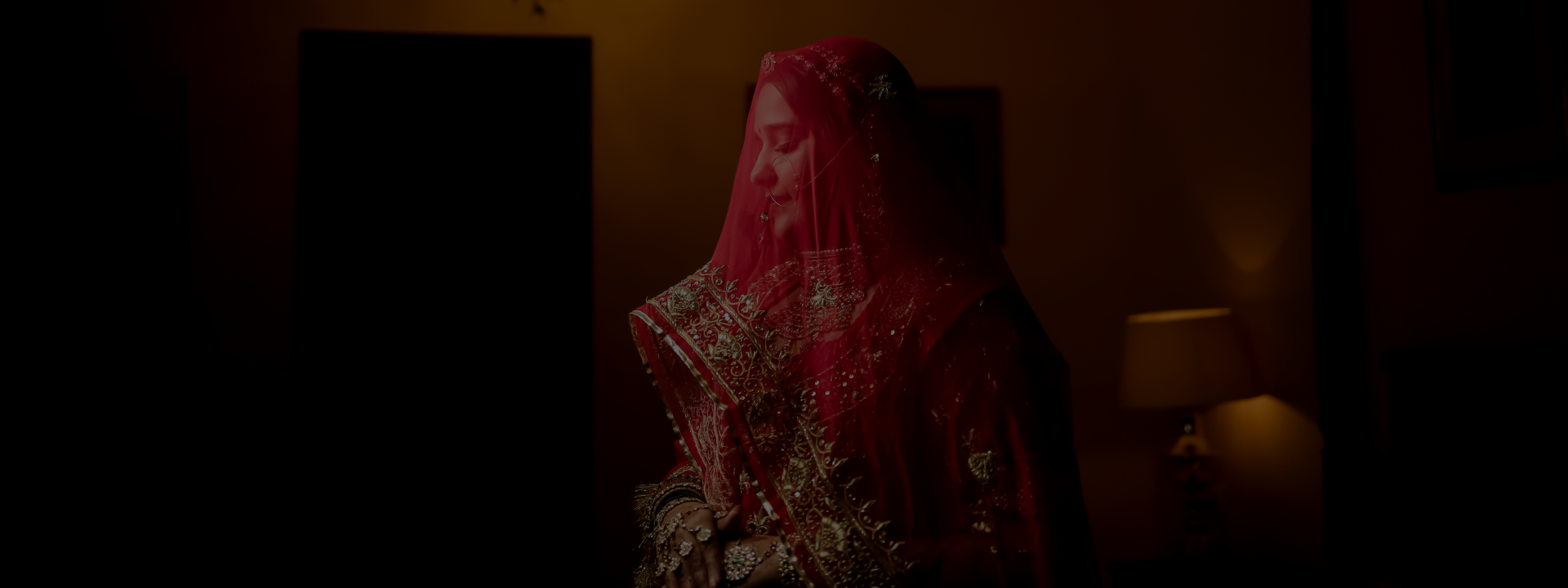 A bride in a striking red veil stands gracefully in a dimly lit setting, creating a captivating and mysterious atmosphere.