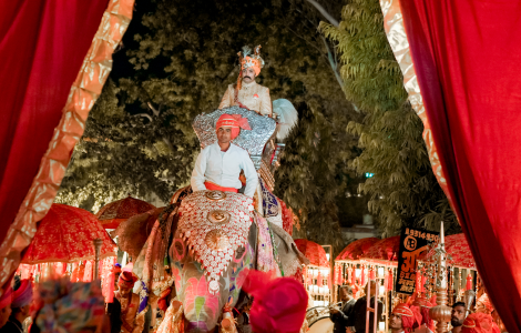 A groom rides an elephant under a striking red tent, showcasing a memorable scene from a wedding celebration.