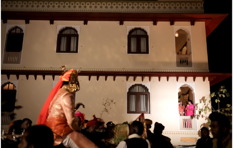  A groom in traditional Indian costume stands proudly before a building, showcasing a beautiful wedding scene.